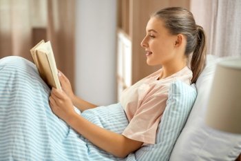 people, bedtime and sleeping concept - smiling girl reading book in bed at home. smiling girl reading book in bed at home