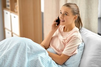 people, communication and technology concept - happy smiling girl with smartphone calling in bed at home. happy girl with smartphone calling in bed at home