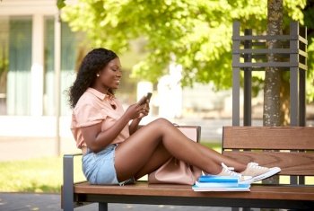 technology, education and people concept - happy smiling african american student girl with smartphone and books in city. african student girl with smartphone in city