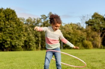 childhood, leisure and people concept - happy african american girl playing with hula hoop at park. happy girl playing with hula hoop at park