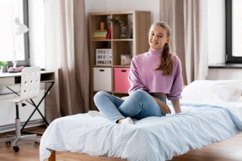 people concept - happy smiling girl sitting on bed at home. happy smiling girl sitting on bed at home