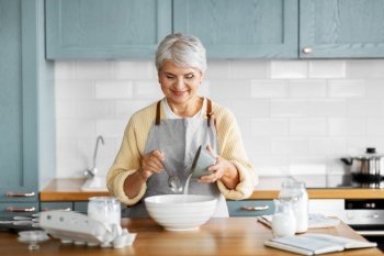 people and culinary concept - happy smiling woman cooking food on kitchen at home and adding sugar. happy woman cooking food on kitchen at home