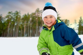childhood, leisure and season concept - happy little boy in winter clothes outdoors over snowy forest or park background. happy little boy in winter clothes outdoors