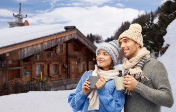 travel, tourism and winter holidays concept - happy romantic couple in knitted hats and scarves with mugs over mountains and ski resort background. happy couple with mugs drinking coffee in winter