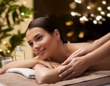 wellness, beauty and relaxation concept - beautiful young woman lying and having massage at spa over garland lights on window background. woman lying and having massage at spa