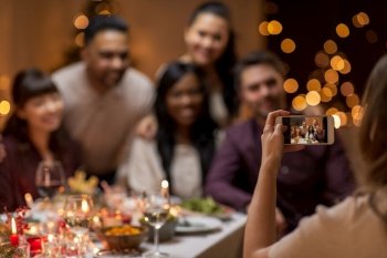 photographing, holidays and celebration concept - close up of woman with smartphone taking picture of her happy friends at christmas dinner. happy friends photographing at christmas dinner