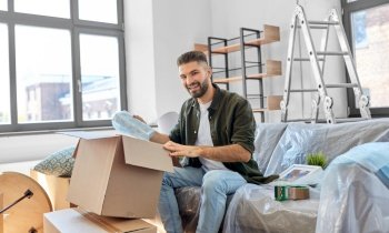 moving, people and real estate concept - happy smiling man unpacking boxes at new home. happy man unpacking boxes and moving to new home