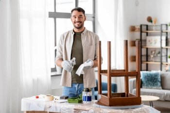 furniture restoration, diy and home improvement concept - happy smiling man applying solvent to rag and renovating old wooden table. man applying solvent to rag for cleaning old table