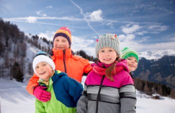 childhood, friendship and season concept - group of happy little kids in winter clothes outdoors over snow-covered mountains or alps on background. happy little kids in winter clothes outdoors