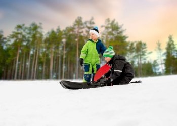 childhood, sledging and season concept - little boys sliding on sleds down snow hill in winter over snowy forest or park background. kids sliding on sleds down snow hill in winter
