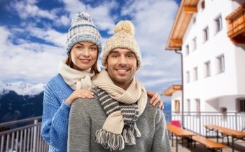 travel, tourism and winter holidays concept - happy couple in knitted hats and scarves over mountains and ski resort background. couple in winter over mountains and ski resort
