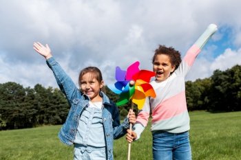 childhood, leisure and people concept - happy girls with pinwheel having fun at park. happy girls with pinwheel having fun at park