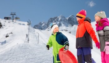 childhood, sledging and season concept - group of happy little children with sleds in winter over alps mountains on background. happy little children with sleds in winter