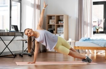 sport, fitness and healthy lifestyle concept - smiling teenage girl exercising on yoga mat and doing plank at home. happy teenage girl exercising on yoga mat at home