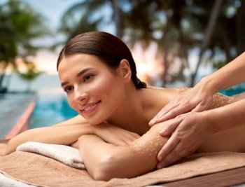 wellness, beauty and relaxation concept - happy young woman having exfoliating salt massage at spa over tropical beach background in french polynesia. happy woman having exfoliating salt massage at spa