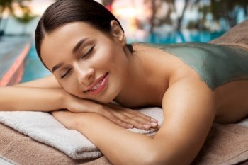 wellness, beauty and cosmetology concept - beautiful young woman lying with blue clay mask at spa over tropical beach background in french polynesia. woman with blue clay mask in spa over beach