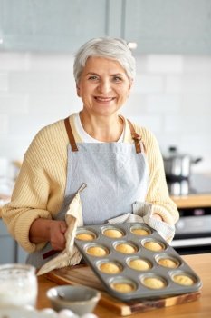 cooking, food and culinary concept - happy smiling senior woman with cupcakes in baking mold on kitchen at home. woman with cupcakes in baking mold on kitchen