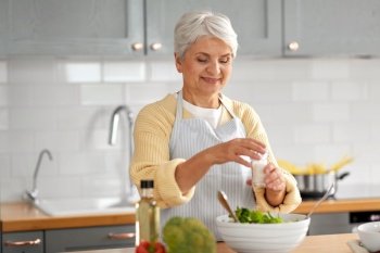 healthy eating, food cooking and culinary concept - happy smiling senior woman with salt making vegetable salad on kitchen at home. happy woman cooking salad on kitchen at home