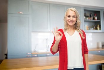 cooking, culinary and people concept - happy smiling young woman in red cardigan showing ok hand sign over kitchen background. happy young woman showing ok hand sign on kitchen