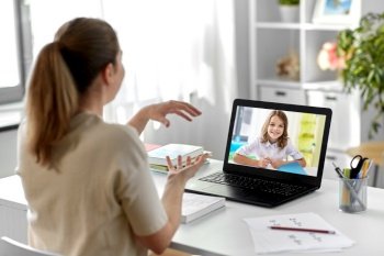 distant education, remote job and people concept - happy smiling female teacher with student girl on laptop computer screen having video call or online class at home office. teacher with laptop having video call at home