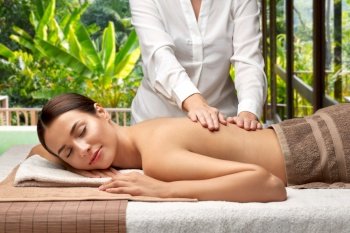 wellness, beauty and relaxation concept - beautiful young woman lying and having back massage at spa over bungalow at exotic resort in thailand on background. woman lying and having back massage at spa