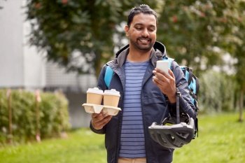 food shipping, profession and people concept - happy smiling delivery man with thermal insulated bag and takeaway coffee cups using smartphone on city street. food delivery man with takeaway coffee and phone