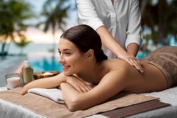 wellness, beauty and relaxation concept - beautiful young woman lying and having back massage at spa over tropical beach background in french polynesia. woman lying and having back massage at spa