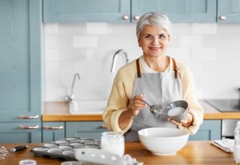 people and culinary concept - happy smiling woman cooking food on kitchen at home and adding sugar. happy woman cooking food on kitchen at home