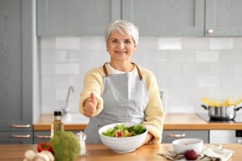 healthy eating, food cooking and culinary concept - happy smiling senior woman making vegetable salad and showing thumbs up on kitchen at home. happy woman cooking salad and showing thumbs up