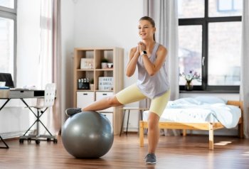 sport, fitness and healthy lifestyle concept - smiling teenage girl exercising with exercise ball at home. teenage girl training on exercise ball at home
