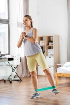 sport, fitness and healthy lifestyle concept - legs of young woman or teenage girl exercising with resistance band at home. woman exercising with resistance band at home