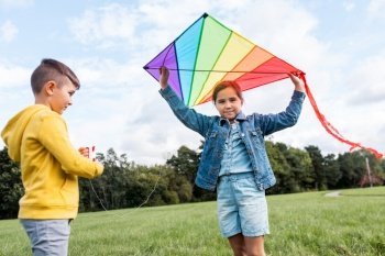 childhood, leisure and people concept - happy boy and girl with kite playing at park. happy boy and girl with kite playing at park