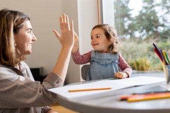 family, motherhood and leisure concept - mother spending time with her little daughter and making high five gesture at home. mother with daughter drawing and making high five