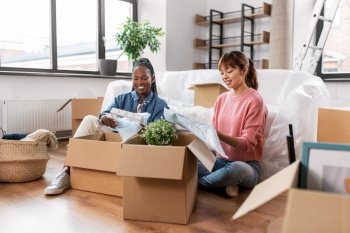 moving, people and real estate concept - happy smiling women packing or unpacking boxes at home. women unpacking boxes and moving to new home