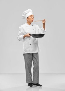 food cooking, culinary and people concept - female chef with frying pan blowing to spoon over grey background. female chef with frying pan blowing to spoon
