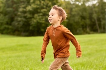 childhood, leisure and people concept - happy little boy running at park. happy little boy running at park