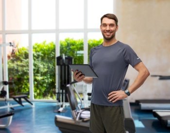 fitness, sport and healthy lifestyle concept - smiling man in sports clothes holding tablet pc computer over gym background. smiling man holding tablet pc in gym