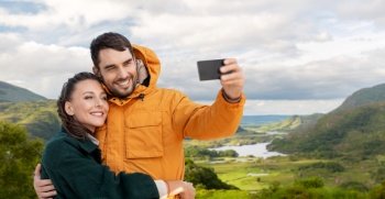 technology, travel and travel concept - happy couple with smartphone over river valley at Killarney National Park in ireland on background. couple taking selfie on phone over irish landscape