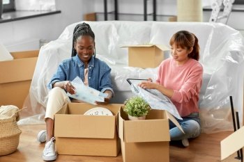 moving, people and real estate concept - women unpacking boxes at new home or packing stuff into bubble wrap. women unpacking boxes and moving to new home