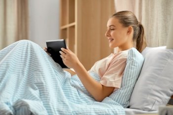 people, bedtime and rest concept - happy smiling girl with tablet pc computer lying in bed at home. happy girl with tablet pc computer in bed at home
