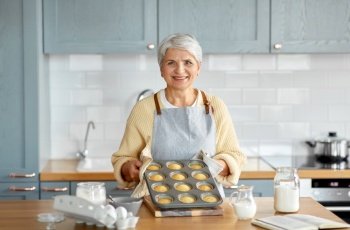 cooking, food and culinary concept - happy smiling senior woman with cupcakes in baking mold on kitchen at home. woman with cupcakes in baking mold on kitchen