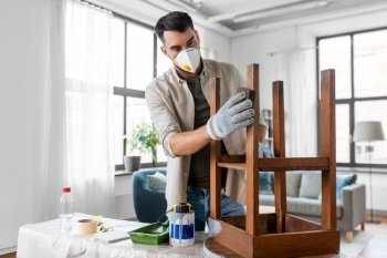 furniture renovation, diy and home improvement concept - man in respirator and gloves sanding old round wooden table with sponge. man in respirator sanding old table with sponge