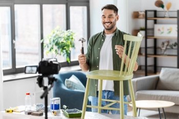 blogging, furniture restoration and home improvement concept - happy smiling man or blogger with camera, hammer and nail showing old wooden chair renovation and recording tutorial video. male blogger with hammer showing chair renovation