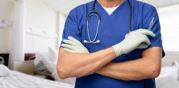 healthcare, vaccination and medicine concept - close up of doctor or male nurse in blue uniform and protective medical gloves with stethoscope and syringe over hospital ward background. close up of male doctor in gloves with syringe