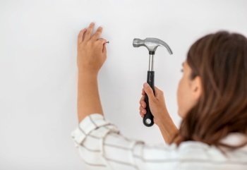 home improvement, repair and people concept - close up of woman hammering nail to wall. close up of woman hammering nail to wall at home
