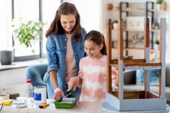 renovation, diy and home improvement concept - happy smiling mother and daughter in gloves with paint roller painting old wooden table in grey color at home. mother and daughter painting old table in grey