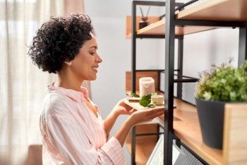 home improvement and decoration and people concept - happy smiling young woman placing candles with eucalyptus branch to shelf. happy woman decorating home with candles