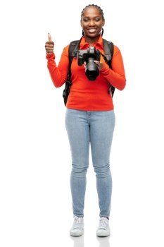 people, profession and photography concept - happy smiling woman photographer with digital camera and backpack showing thumbs up over white background. woman with camera and backpack showing thumbs up