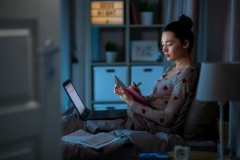 education, technology and people concept - teenage student girl with notebook and laptop computer learning in bed at home at night. student girl with notebook and laptop at night