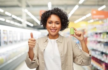 shopping and consumption concept - smiling woman holding alkaline battery over supermarket background. smiling woman with alkaline battery at supermarket